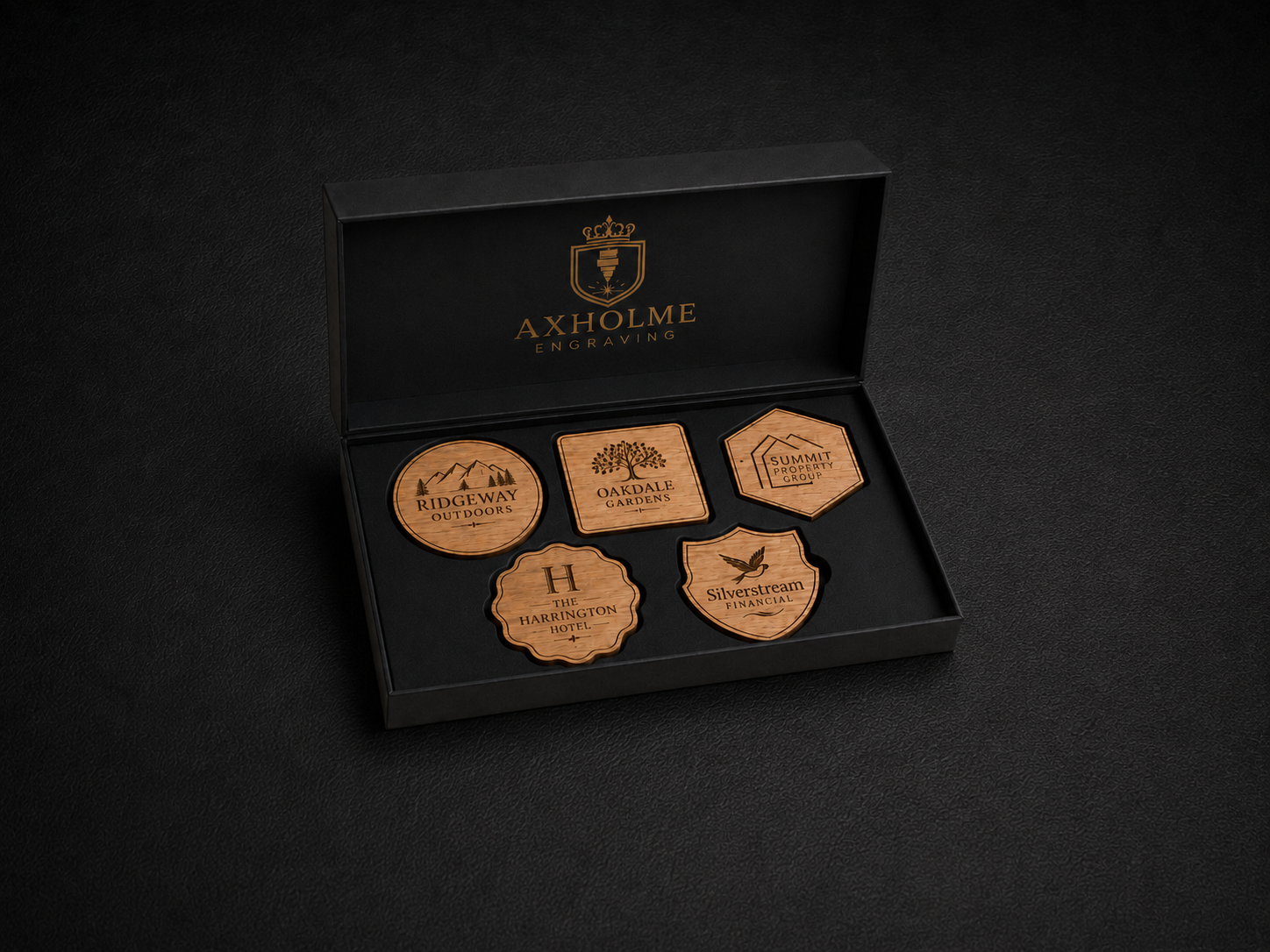 An open black presentation box on a dark background, containing five engraved wooden brand tokens or coasters. The inside lid shows the visible brand name AXHOLME ENGLAND in gold lettering with a crest above it.