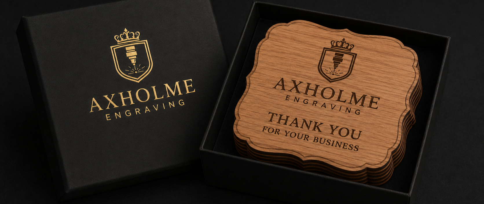 A set of engraved wooden coasters displayed in an open black presentation box next to its branded black lid. The coasters are light brown wood with black engraved text reading 'AXHOLME ENGRAVING' and 'THANK YOU FOR YOUR BUSINESS'.
