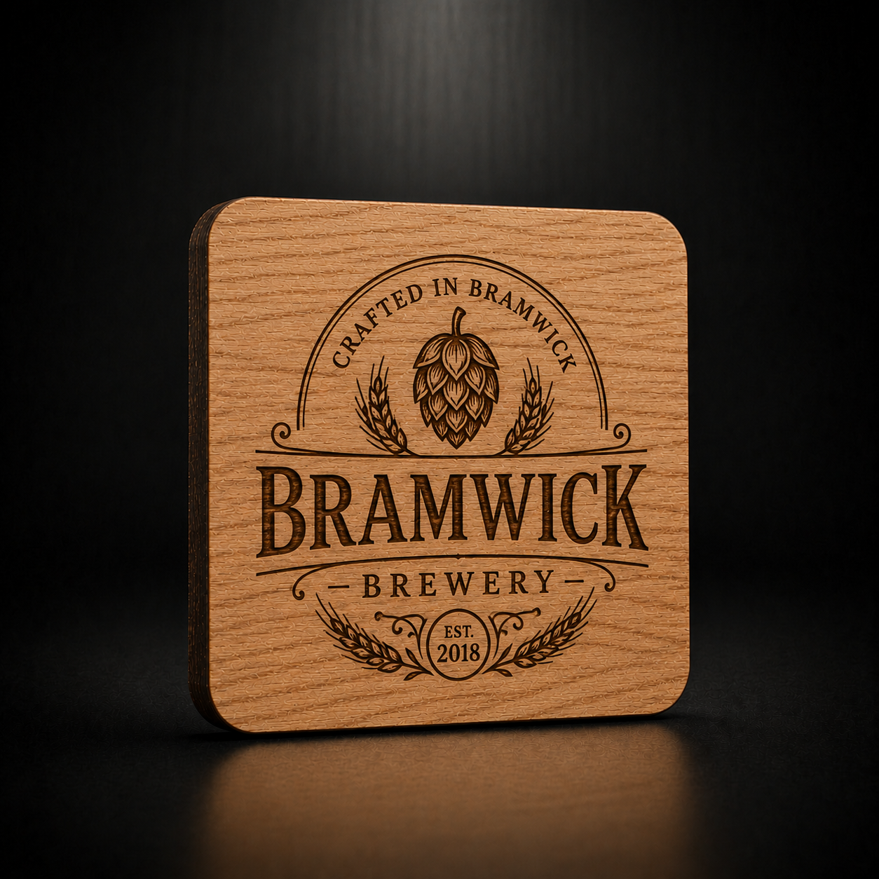 A square wooden coaster with rounded corners featuring a laser-engraved Bramwick Brewery logo, set against a dark, reflective background.