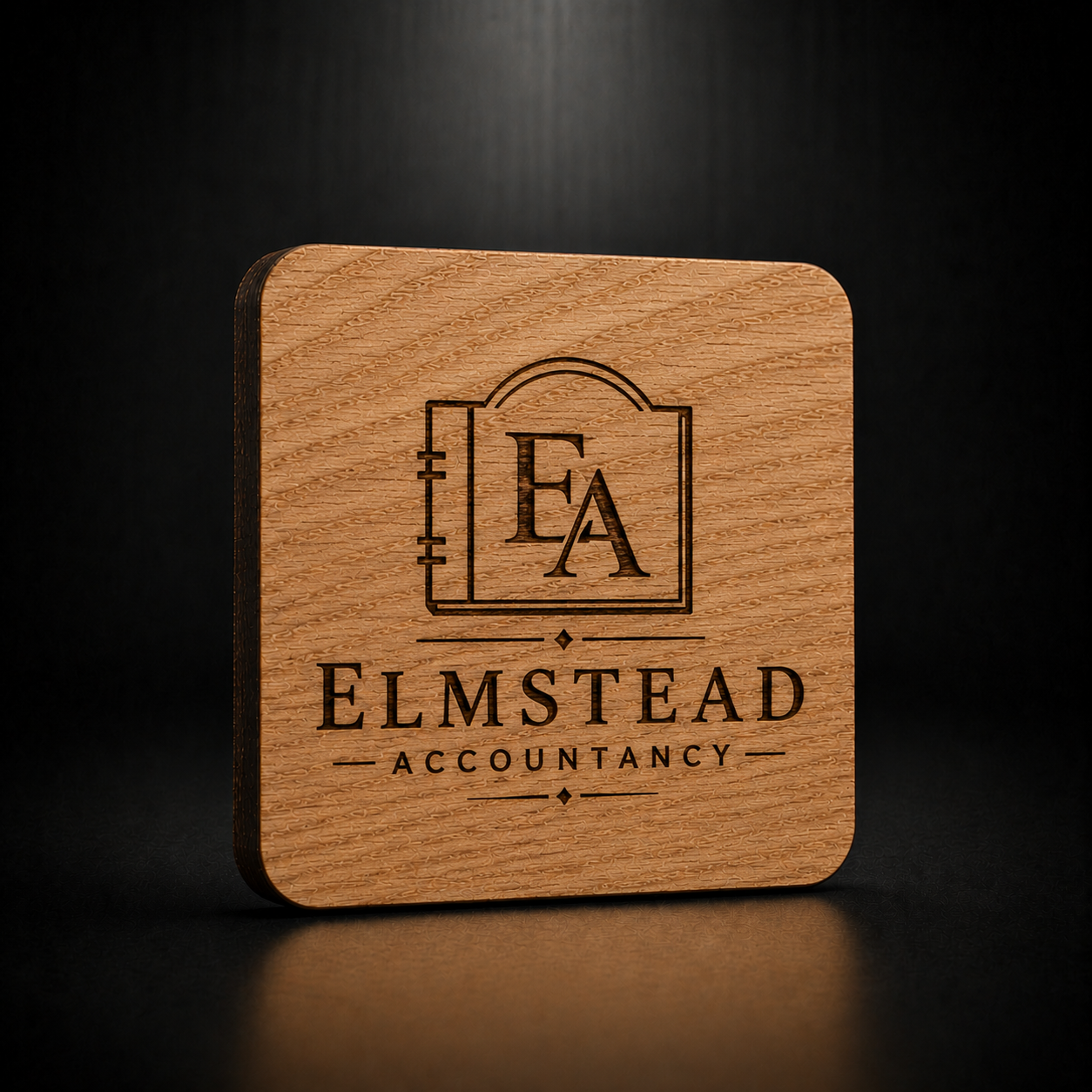 A square wooden plaque or coaster with rounded corners, featuring a laser-engraved logo of an open book with the letters 'EA' and the text 'ELMSTEAD ACCOUNTANCY' on a dark, reflective background.