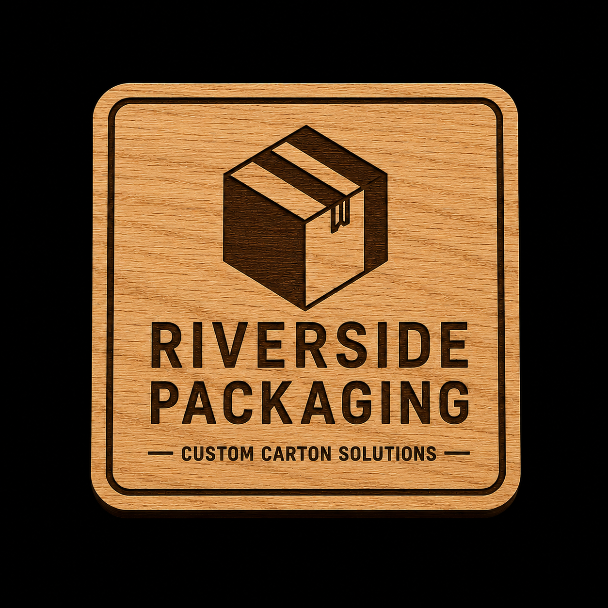 A square wooden plaque or sign with rounded corners featuring a dark brown engraved box icon and the text 'RIVERSIDE PACKAGING' and 'CUSTOM CARTON SOLUTIONS' on a black background.