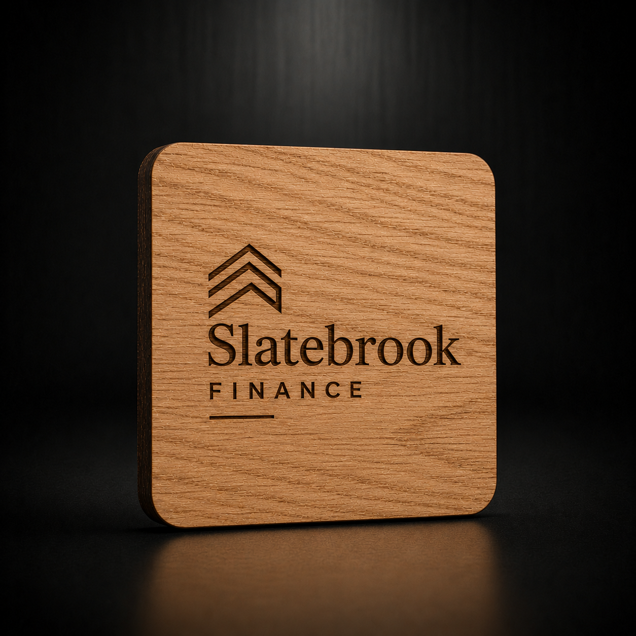 A square wooden plaque or coaster with rounded corners, featuring the engraved Slatebrook Finance logo and text on a dark, reflective surface.
