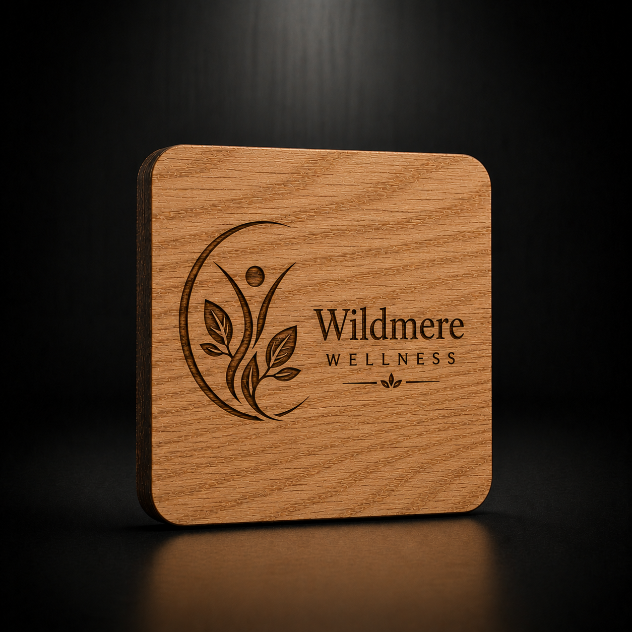A square wooden coaster with rounded corners, featuring a laser-engraved logo for 'Wildmere Wellness' on a dark wood surface, set against a dark background.