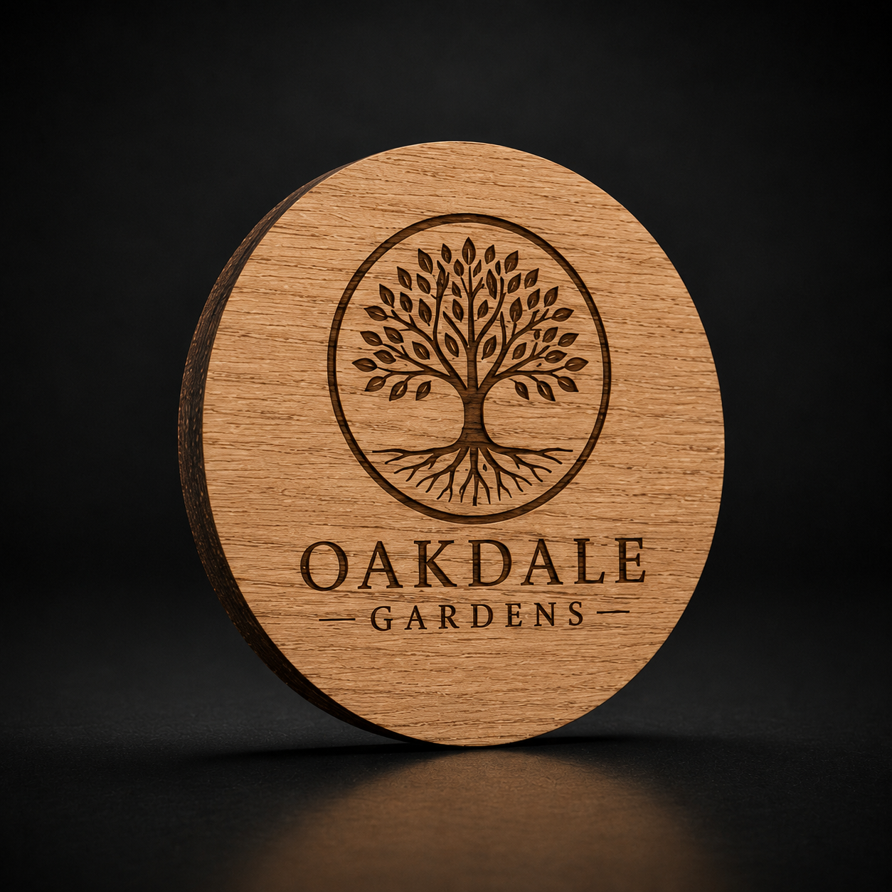 A round wooden coaster featuring a laser-engraved tree of life logo and the text 'OAKDALE GARDENS', set against a dark background.